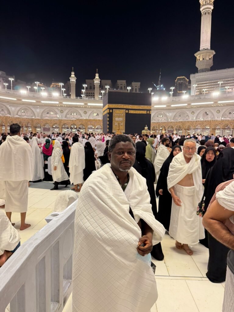 A Kasfah Hajj Umrah guest pauses for a photo as worshippers circle the Kaaba at night in Makkah